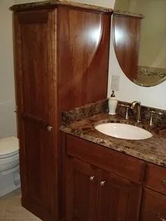 Wood bathroom vanity with marble countertop, oval sink, mirror, and dark wood cabinet storage