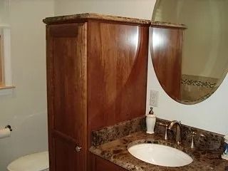 Small bathroom with wooden vanity, round mirror, and toilet visible.