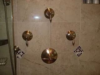 Shower with five brass control knobs on beige tiled wall, with small decorative tile accents