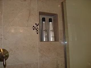 Bathroom shower wall with built-in niche holding two silver bottles and a small decorative tile accent