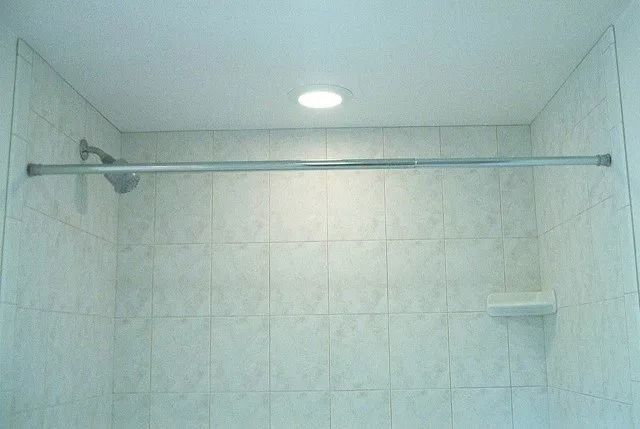 Empty tiled shower with a metal curtain rod and small wall shelf