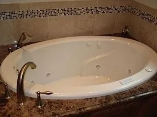 Oval bathtub with brass fixtures set into a tiled bathroom corner