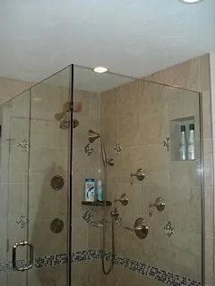 Glass-enclosed shower with multiple chrome showerheads and beige tile walls