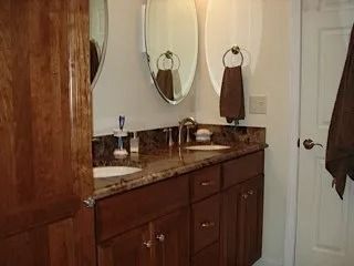 Bathroom vanity with double mirrors, brown cabinets, and a granite countertop.