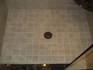 Beige tiled shower floor with a central drain and dark trim edges.