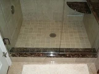 Empty beige tiled walk-in shower with glass curb and drain.