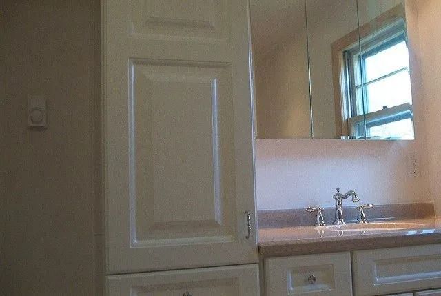 Bathroom vanity with sink, mirror, and beige cabinets near a window