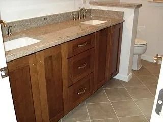 Bathroom vanity with double sink, wood cabinets, granite countertop, and tiled floor.