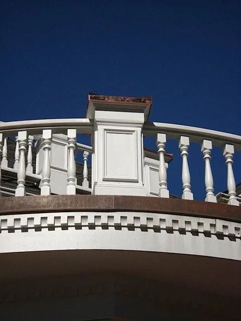White balcony railing with decorative balusters against a clear blue sky