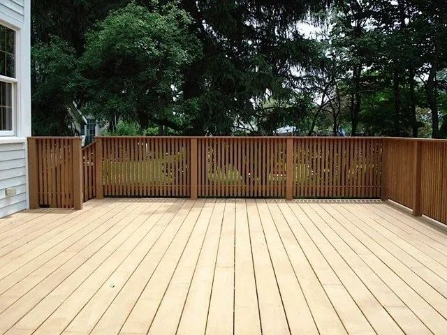 Wooden backyard deck with a slatted railing and trees in the background