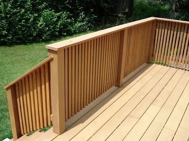Wooden deck with light tan railings and steps overlooking a green lawn and hedge