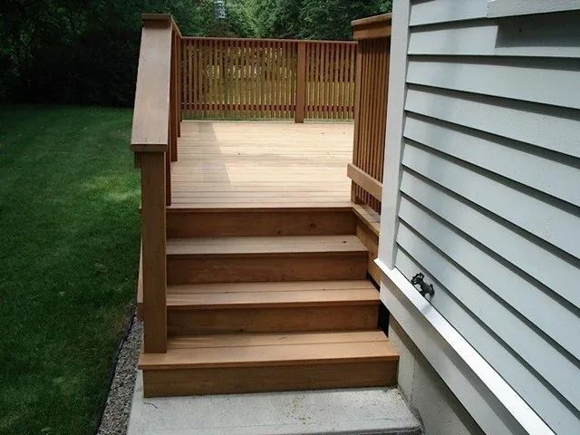 Wooden back deck with stairs beside white siding and a grassy yard