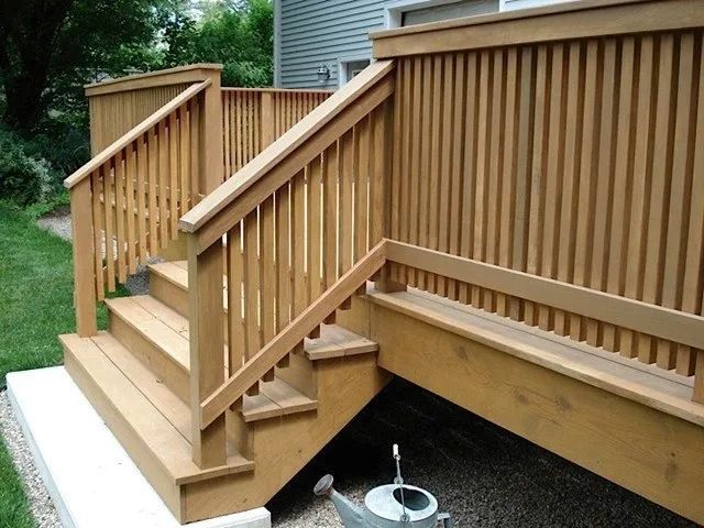 Wooden deck stairs with railings leading to a raised porch, with grassy yard below.