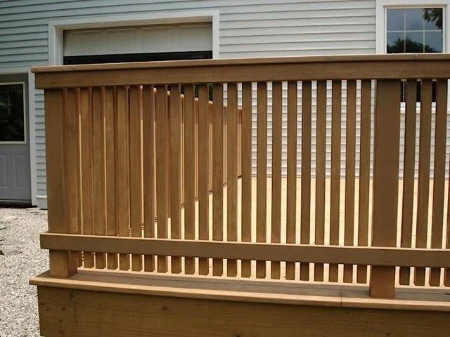 Wooden railing on a raised porch in front of a beige house exterior