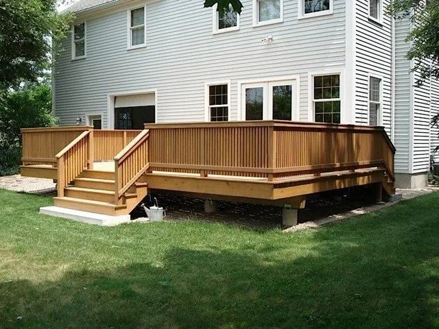 Wooden backyard deck with stairs attached to a beige house, overlooking a grassy lawn.