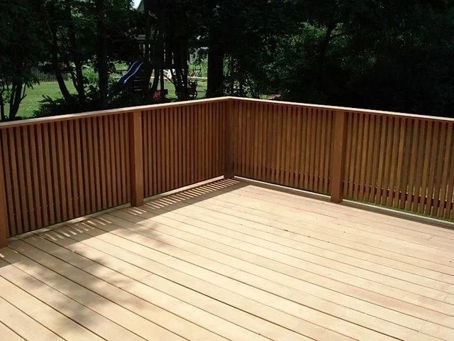 Wooden deck with railing, overlooking a wooded yard in daylight