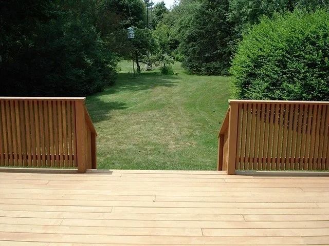 Wooden deck overlooking a grassy path between dense green trees and hedges