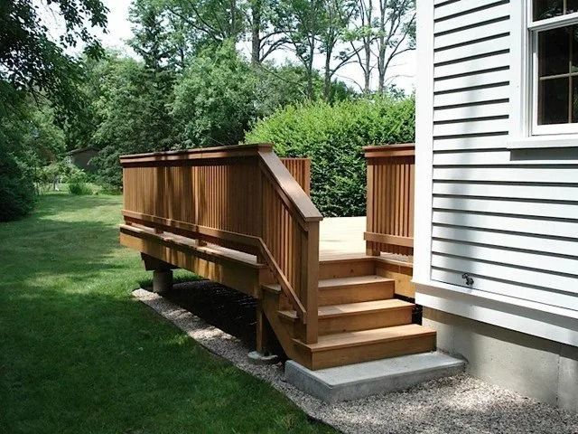 Wooden accessibility ramp with railings beside a white house, leading to a small porch in a grassy yard