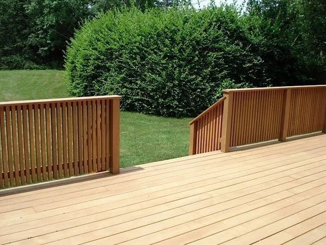 Wooden deck with railings overlooking a grassy yard and dense green bushes