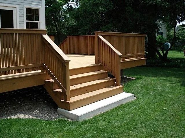 Wooden accessible deck stairs with railings leading down to a green lawn beside a house