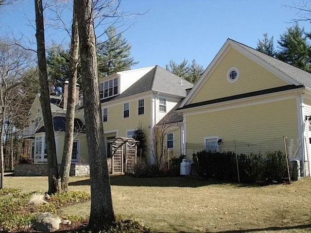Yellow house with white trim, a side addition, and trees in a sunny yard
