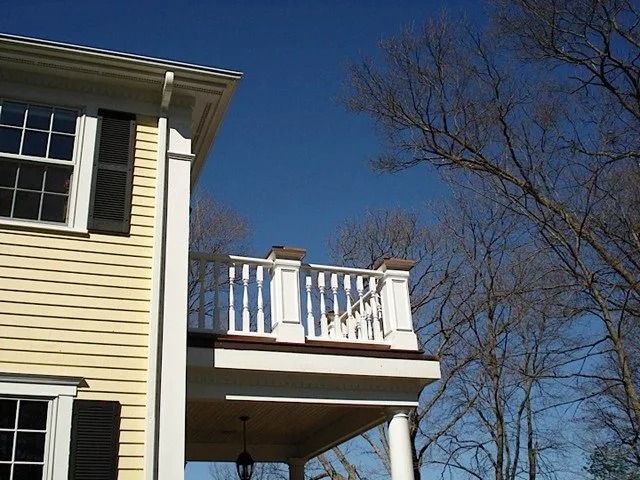 Side of a cream house with a small white-railed balcony against a clear blue sky