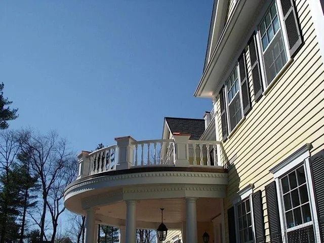 Yellow house with white trim and round porch under a clear blue sky