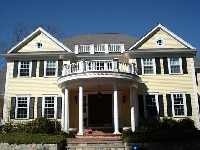 Large yellow colonial-style house with white columns, black shutters, and a curved front porch