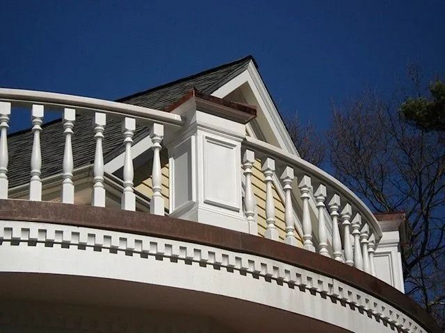White balcony railing and trim on a curved house exterior against a clear blue sky