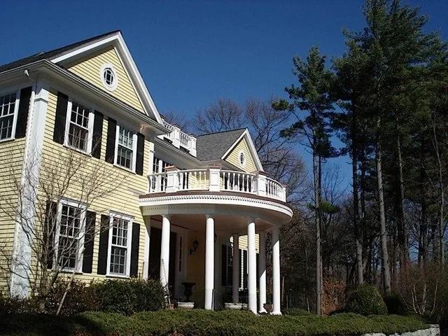 Large yellow house with white columns and a curved porch under a clear blue sky