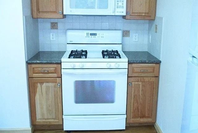 Small kitchen with white gas stove, wooden cabinets, and gray countertops.