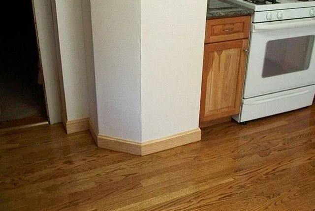 Wooden kitchen floor beside white stove and cabinet, with a doorway and wall corner.
