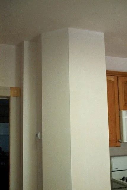 Interior with a large beige column in a room beside a kitchen cabinet.