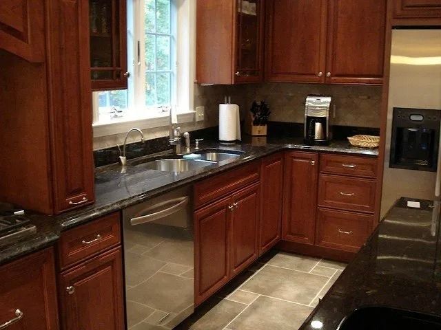 Modern kitchen with cherry cabinets, black countertops, stainless appliances, and tiled floor