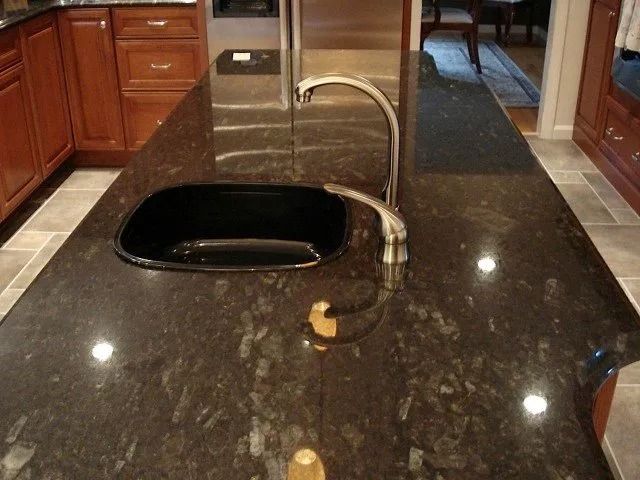 Kitchen island with dark granite countertop, black sink, and curved chrome faucet in a home kitchen.