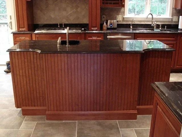 Kitchen island with dark wood panels and black granite countertop, centered in a bright kitchen