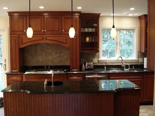 Modern kitchen with dark wood cabinets, black granite island, pendant lights, and a window over the sink