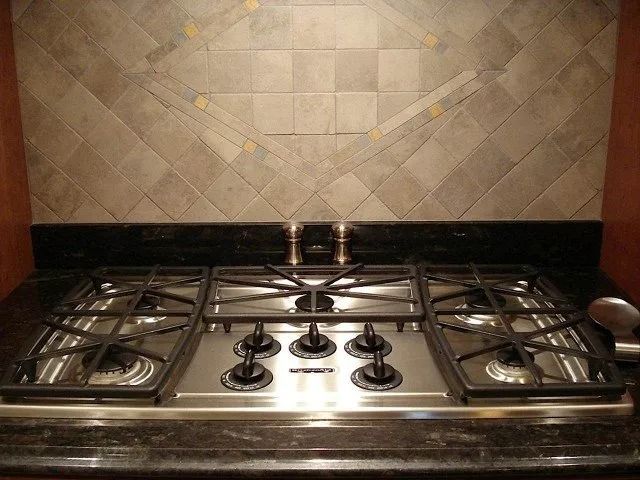 Stainless steel gas stovetop with four burners against a beige tiled kitchen backsplash.