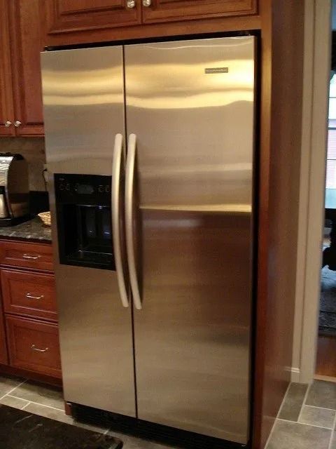 Stainless steel side-by-side refrigerator in a kitchen with wood cabinets and a tiled floor