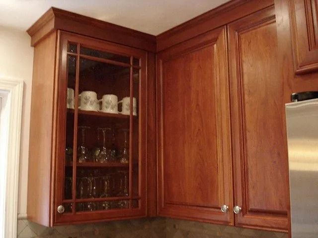 Wooden kitchen cabinets with a glass-front corner display of dishes and stemware