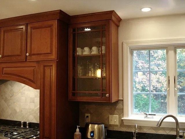 Kitchen with wooden cabinets, tiled backsplash, window, and stainless steel faucet by a sink.