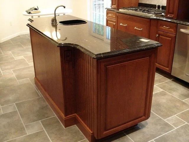 Kitchen island with dark wood cabinets and granite countertop in a tiled kitchen