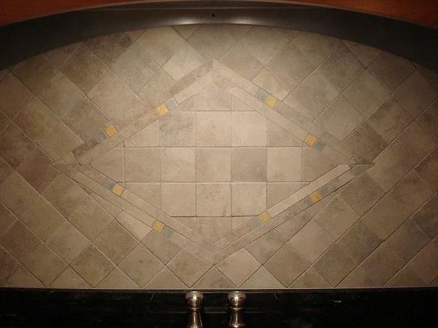 Decorative beige tile wall with a diamond pattern and two metal faucet handles at the bottom