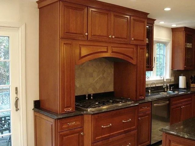Wooden kitchen with dark countertops and a stainless steel stove beneath a carved range hood