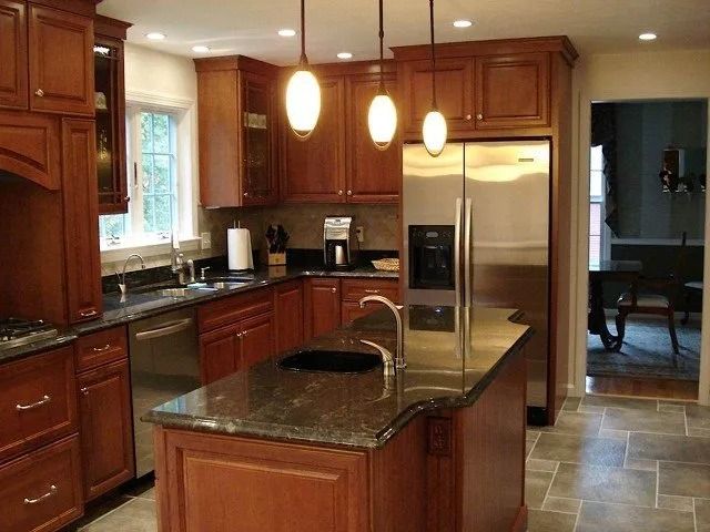 Modern kitchen with wood cabinets, granite island, stainless steel fridge, and pendant lights.