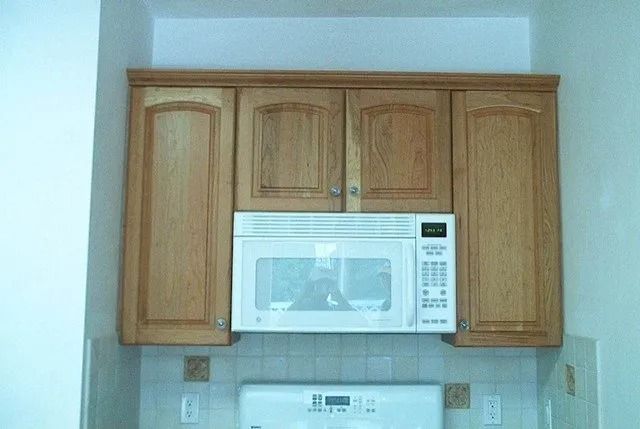 Wooden kitchen cabinets above a white microwave in a light-colored kitchen