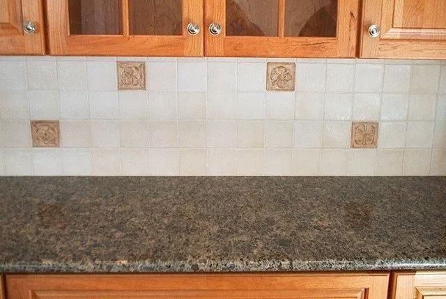 Kitchen countertop with granite surface, tiled backsplash, and wooden cabinets above and below.