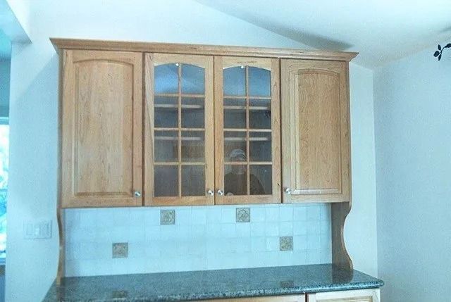 Wooden kitchen cabinets with glass doors above a granite countertop and pale blue wall.