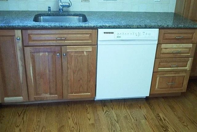 Kitchen cabinets and dishwasher under a countertop with a wood floor