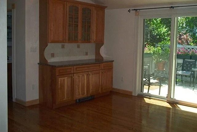 Empty kitchen nook with wooden cabinets and sliding glass door to a patio, hardwood floor.